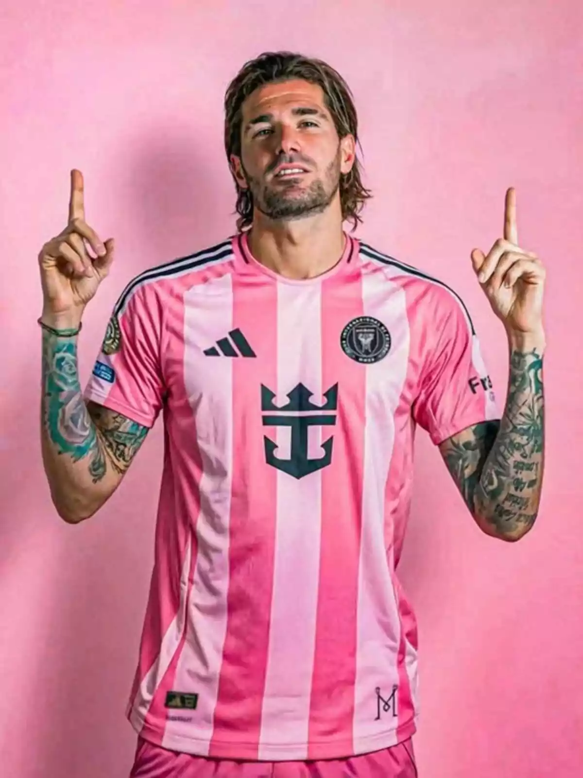 Futbolista con uniforme rosa de Inter Miami posando frente a un fondo del mismo color y levantando ambos dedos índices hacia arriba Futbolista con uniforme rosa de Inter Miami posando frente a un fondo del mismo color y levantando ambos dedos índices hacia arriba