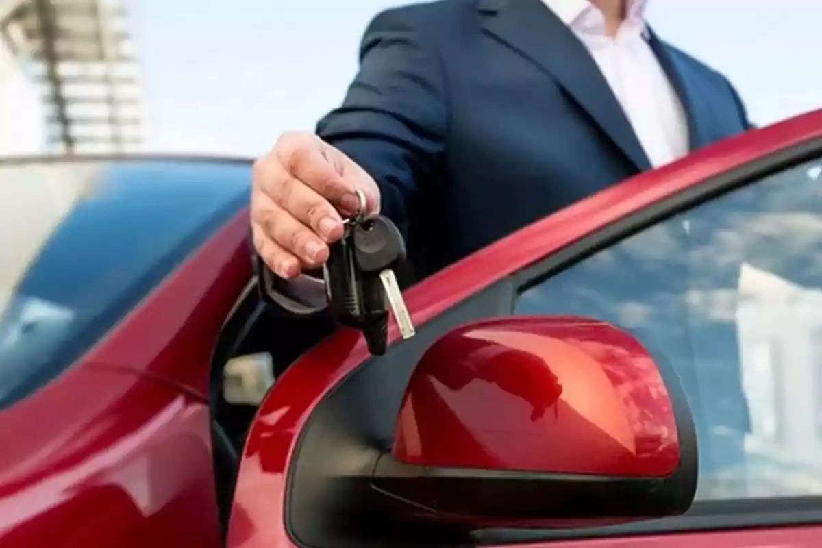 Persona entregando las llaves de un auto rojo mientras está de pie junto a la puerta del vehículo