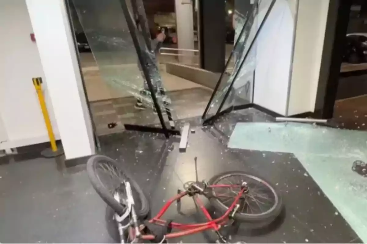 Bicycle lying on the ground in front of a broken glass door with scattered shards and a person in the background Bicycle lying on the ground in front of a broken glass door with scattered shards and a person in the background