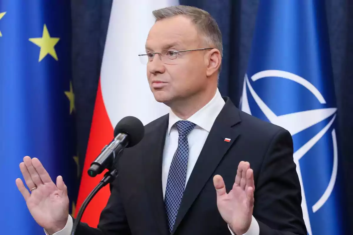 Hombre de traje hablando frente a un micrófono con banderas de la Unión Europea, Polonia y la OTAN al fondo Hombre de traje hablando frente a un micrófono con banderas de la Unión Europea, Polonia y la OTAN al fondo