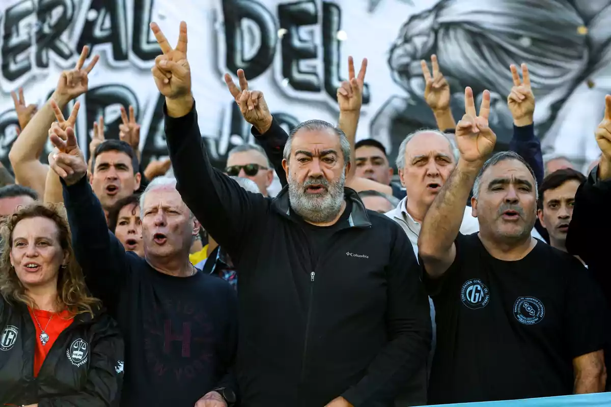 A group of people protesting and raising their hands making the victory sign, with a banner in the background. A group of people protesting and raising their hands making the victory sign, with a banner in the background.