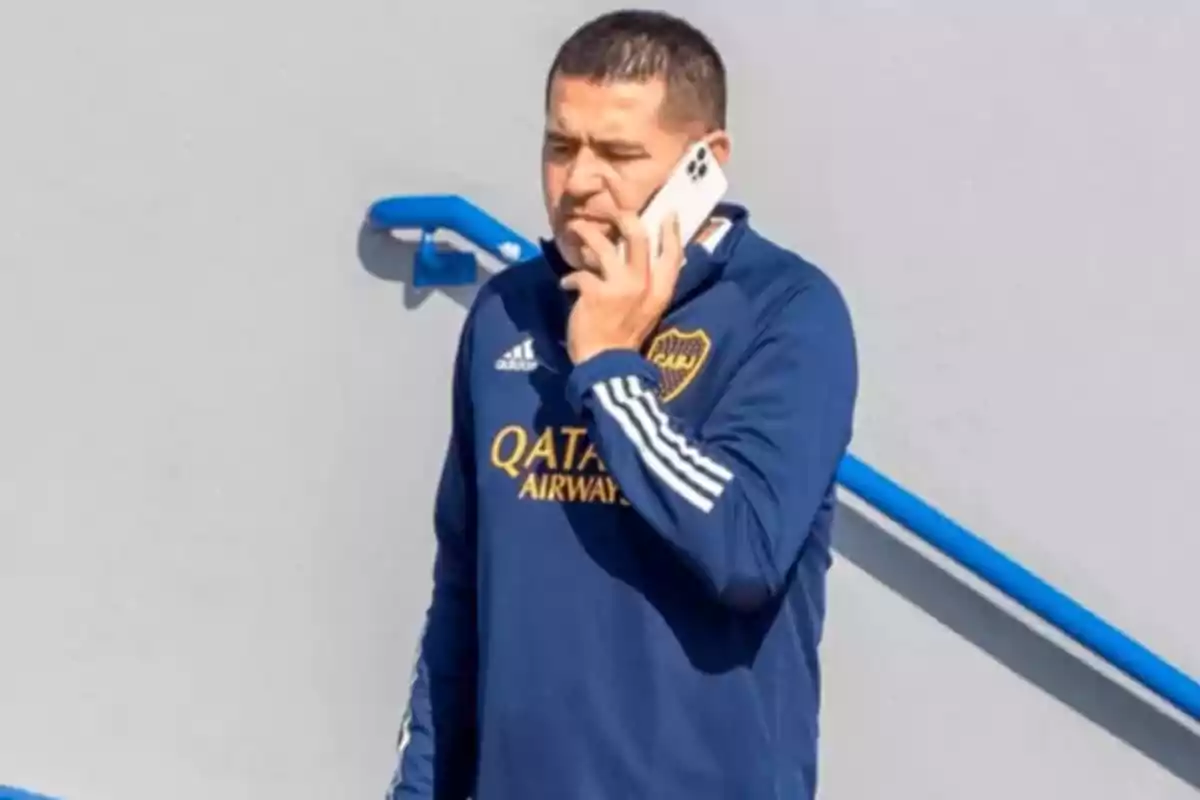 Hombre con buzo azul de Boca Juniors hablando por teléfono móvil junto a una baranda azul