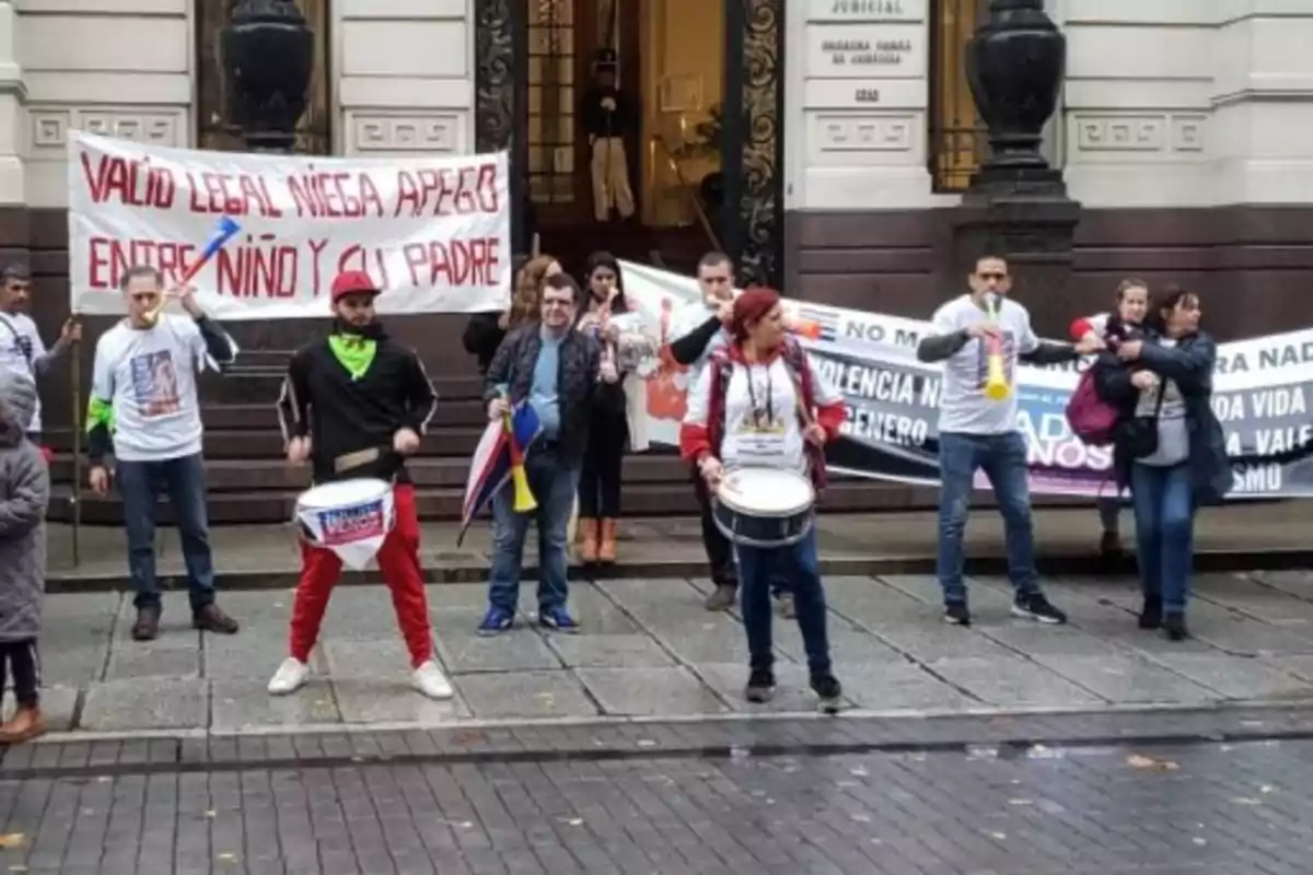 Personas manifestándose frente a un edificio con pancartas y tambores
