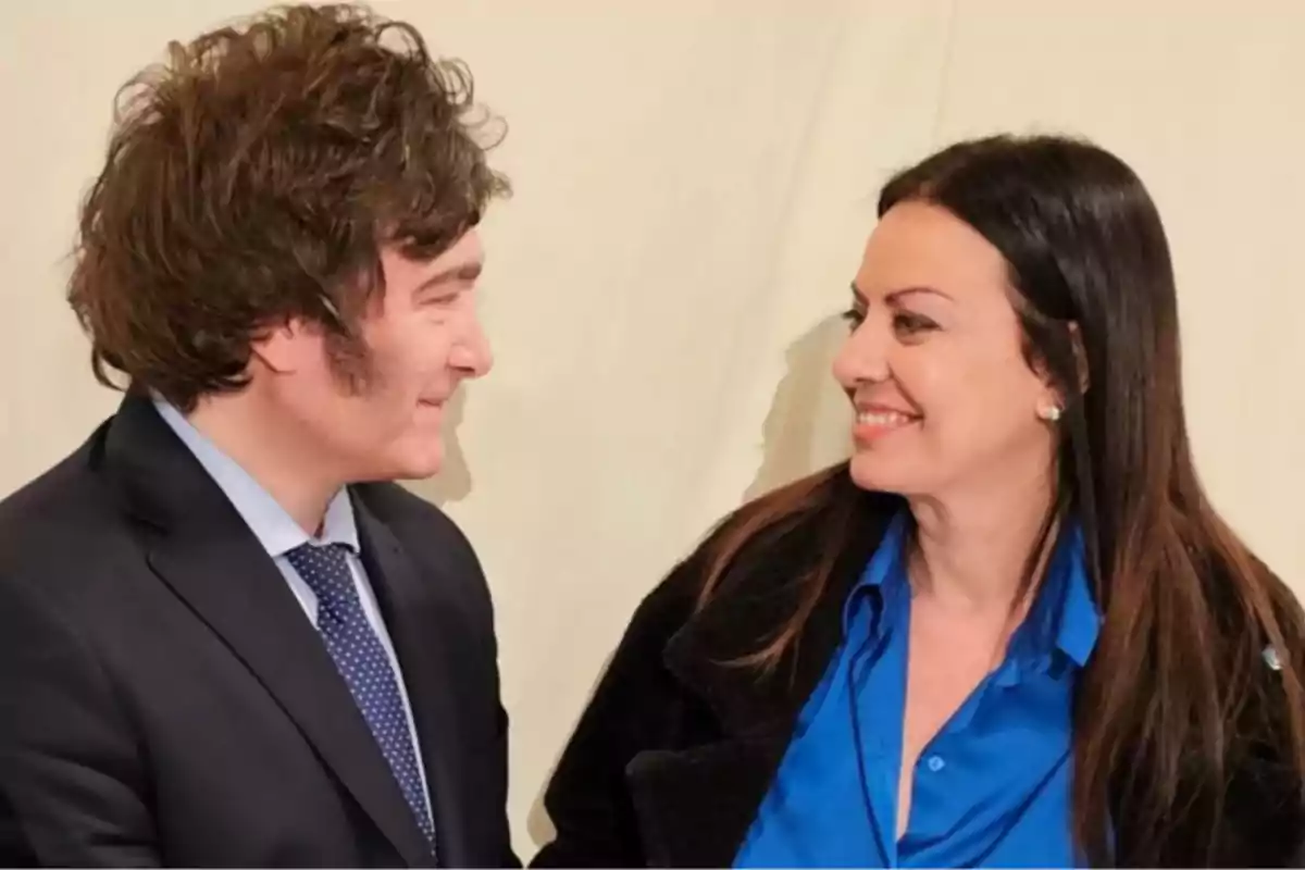Dos personas se miran y sonríen, una lleva traje oscuro y la otra camisa azul Dos personas se miran y sonríen, una lleva traje oscuro y la otra camisa azul