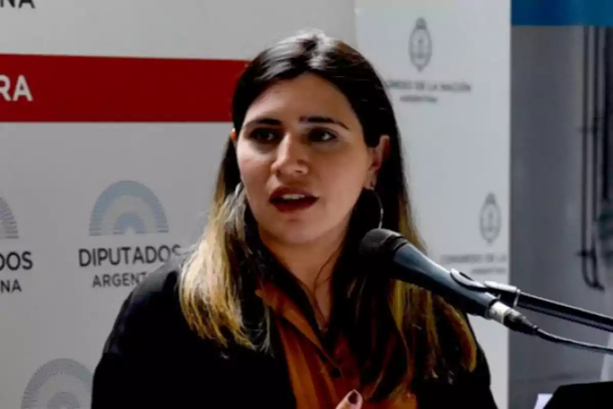 Mujer joven hablando frente a un micrófono en un evento oficial con fondo de logotipos de Diputados de Argentina