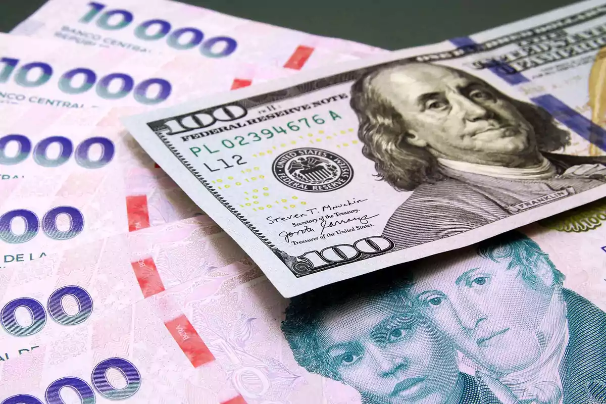 Billetes de cien dólares estadounidenses sobre varios billetes de diez mil pesos chilenos Billetes de cien dólares estadounidenses sobre varios billetes de diez mil pesos chilenos