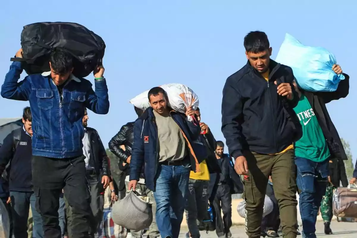 Grupo de personas caminando al aire libre cargando bolsas y mochilas grandes sobre los hombros