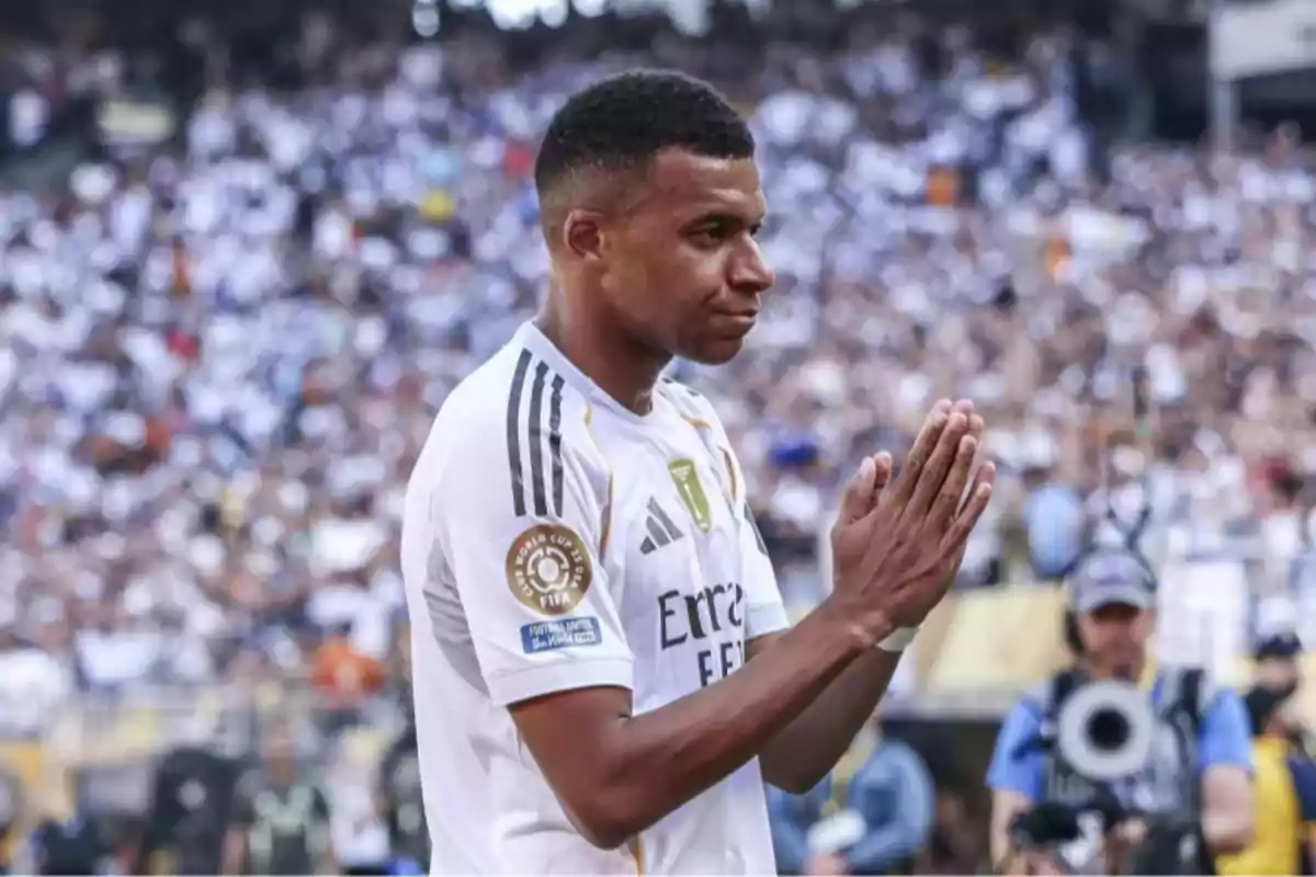 Soccer player in a white uniform applauding in a stadium full of fans