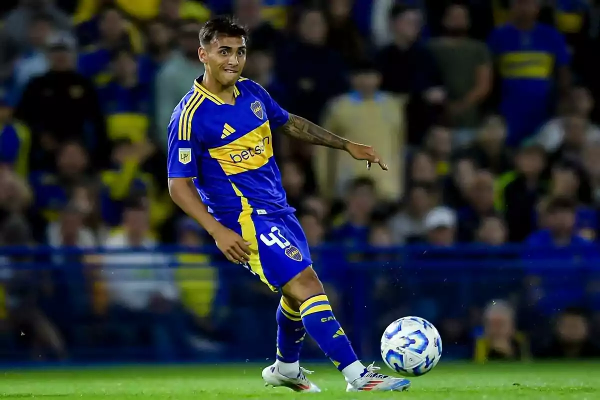 Jugador de Boca Juniors con uniforme azul y amarillo controlando el balón durante un partido de fútbol con público en las gradas de fondo Jugador de Boca Juniors con uniforme azul y amarillo controlando el balón durante un partido de fútbol con público en las gradas de fondo