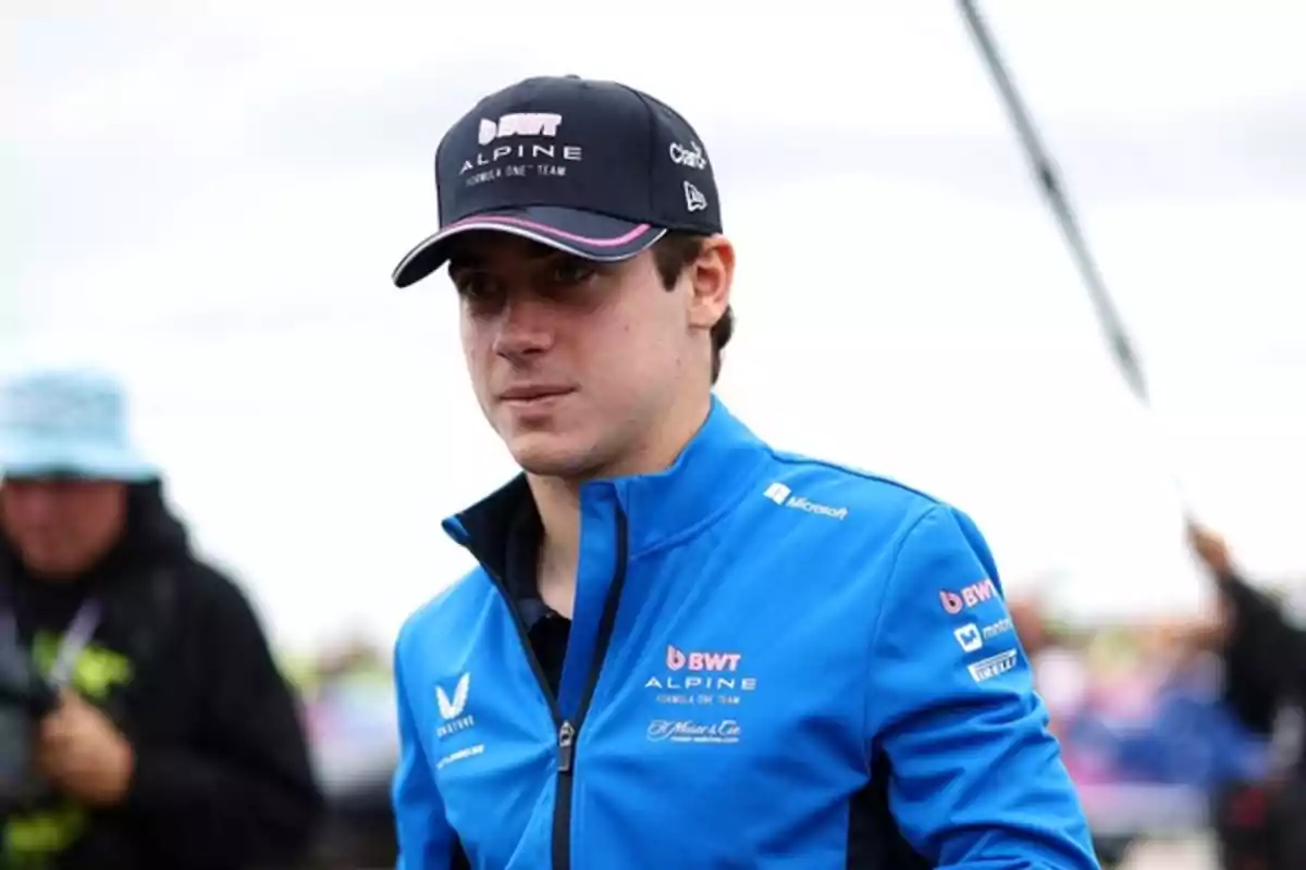 Young man wearing a blue jacket and a black Alpine Formula 1 team cap at an outdoor event Young man wearing a blue jacket and a black Alpine Formula 1 team cap at an outdoor event