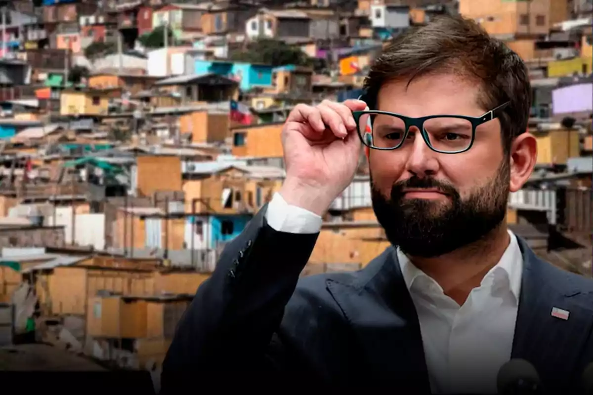 Hombre con barba y gafas ajustándose los lentes frente a un fondo de viviendas precarias