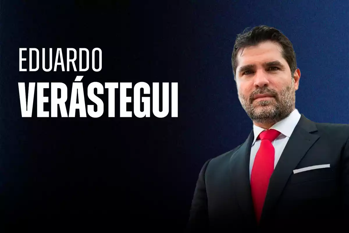 Hombre de barba con traje oscuro y corbata roja posando frente a un fondo azul oscuro con el texto Eduardo Verástegui a la izquierda.