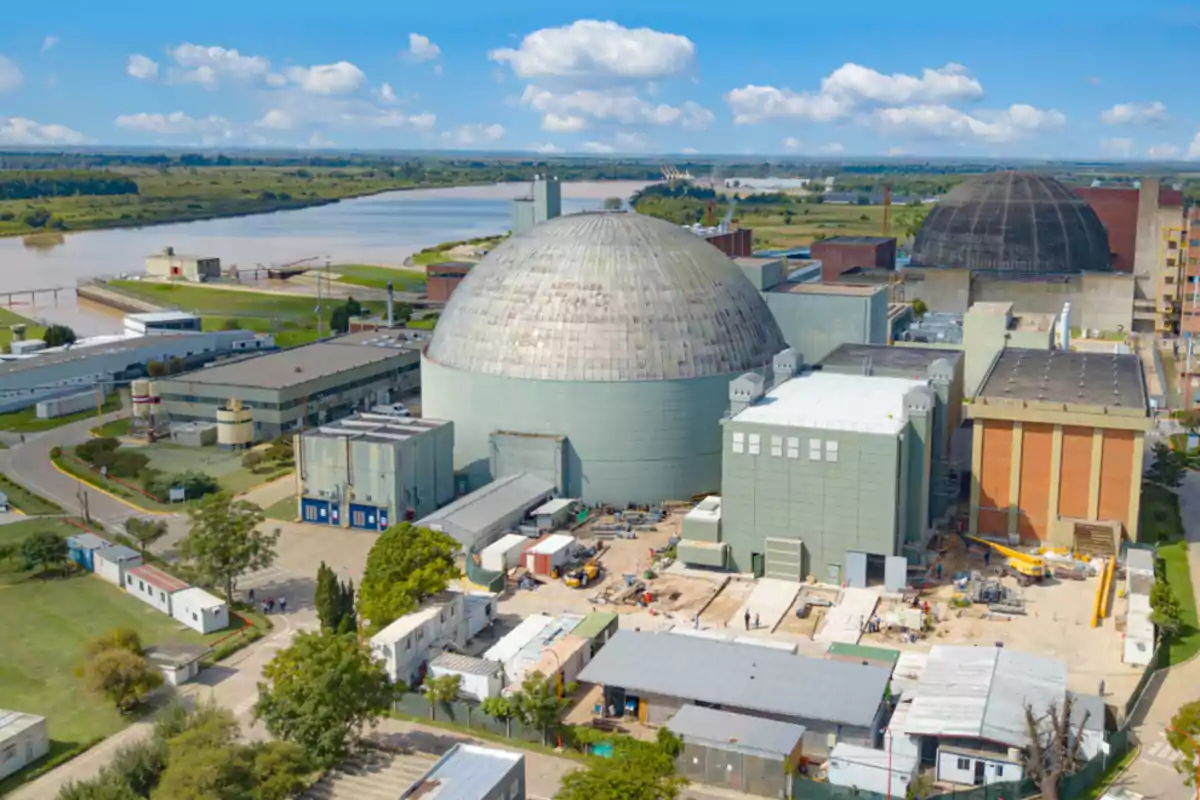 Vista aérea de una planta nuclear junto a un río con cúpulas grandes y edificios industriales rodeados de áreas verdes y caminos