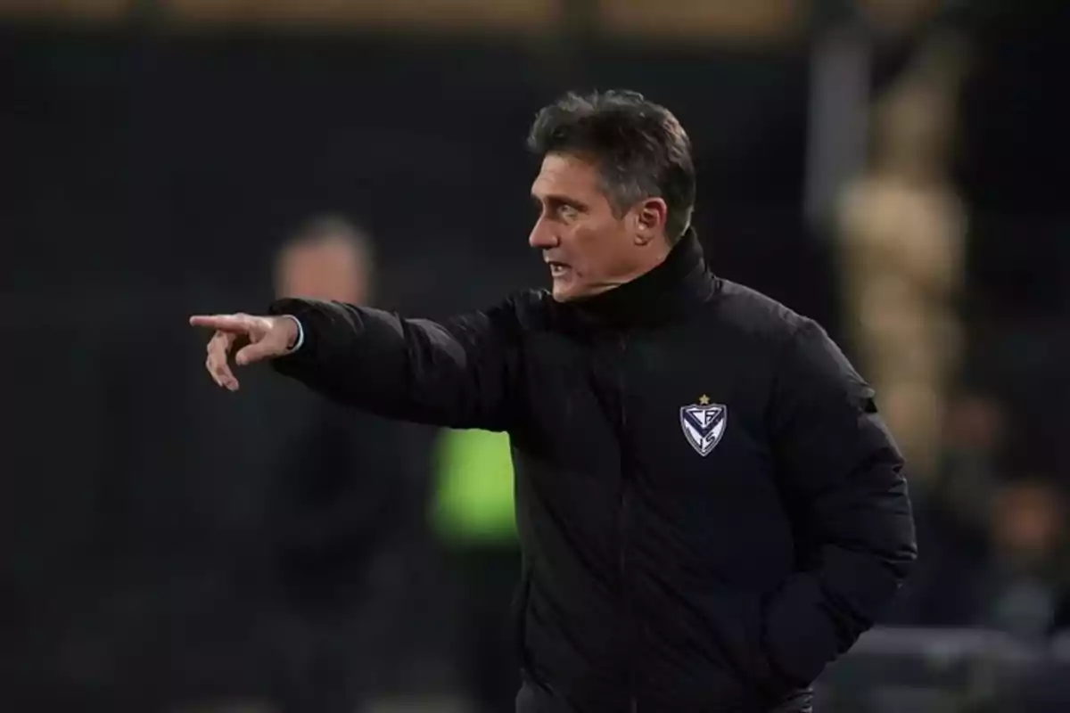 Entrenador de fútbol con chaqueta negra dando indicaciones en la cancha
