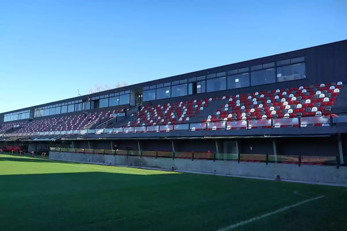 Gradas de un estadio de fútbol con asientos rojos y blancos y una estructura moderna al fondo bajo un cielo despejado Gradas de un estadio de fútbol con asientos rojos y blancos y una estructura moderna al fondo bajo un cielo despejado