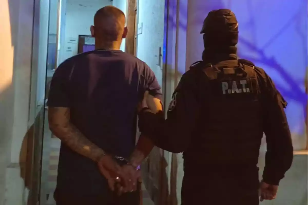 Un policía escolta a un hombre esposado por un pasillo iluminado.
