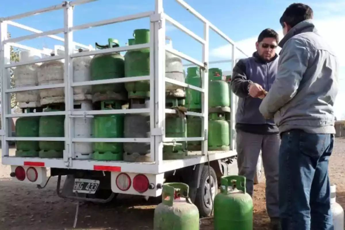 Two people are making a transaction next to a truck loaded with gas canisters.