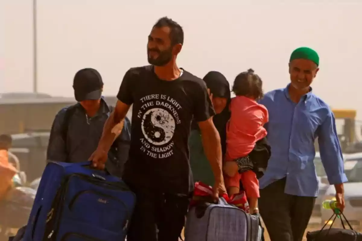 Grupo de personas caminando bajo el sol con maletas y una niña en brazos, aparentan estar en movimiento o migración Grupo de personas caminando bajo el sol con maletas y una niña en brazos, aparentan estar en movimiento o migración