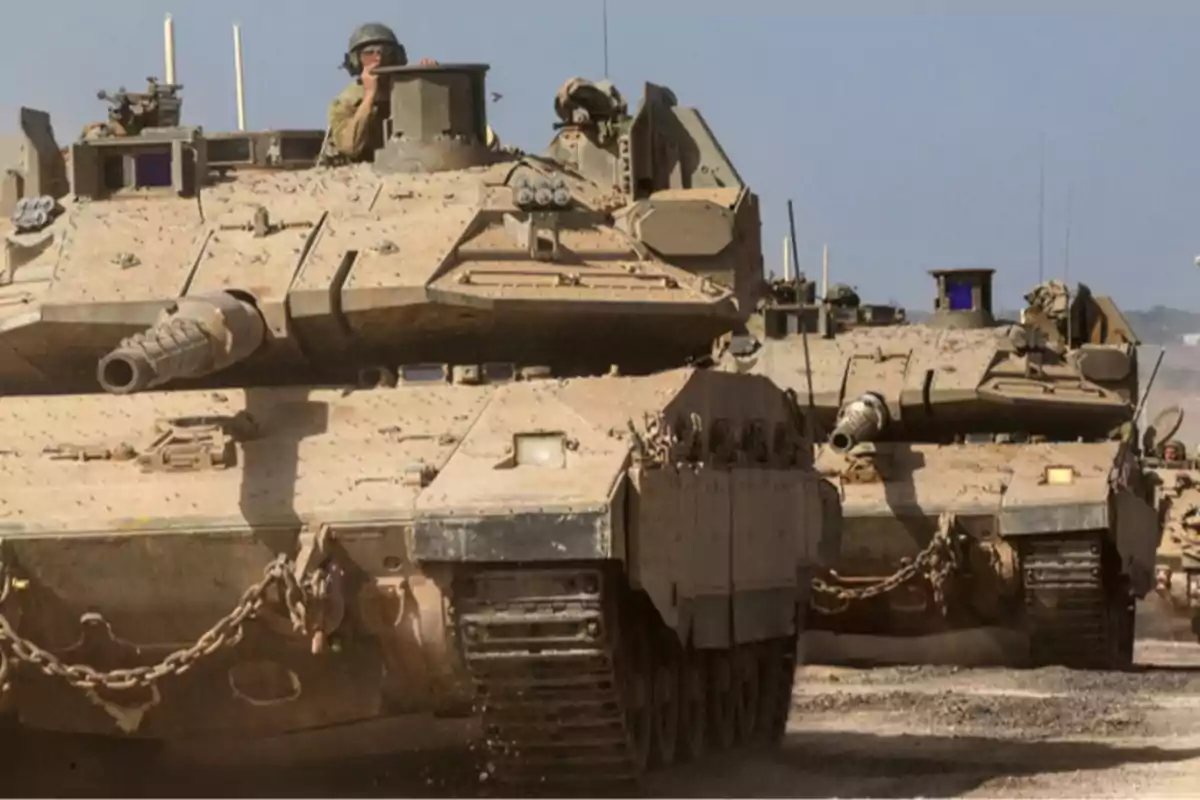 Dos tanques militares avanzan por un terreno polvoriento bajo un cielo despejado mientras soldados asoman por las escotillas Dos tanques militares avanzan por un terreno polvoriento bajo un cielo despejado mientras soldados asoman por las escotillas