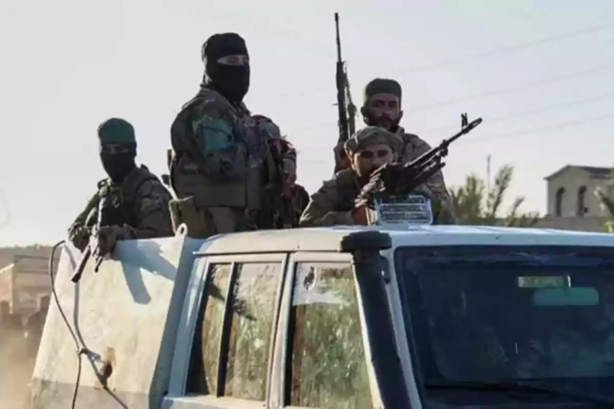 Several armed men wearing military uniforms and with their faces covered are riding in the back of a white pickup truck in an urban area. Several armed men wearing military uniforms and with their faces covered are riding in the back of a white pickup truck in an urban area.