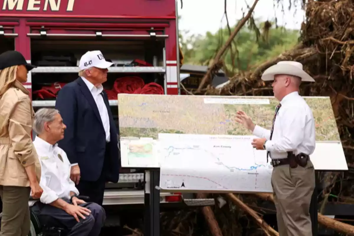Varias personas observan y discuten un mapa grande frente a un camión de bomberos y escombros al aire libre