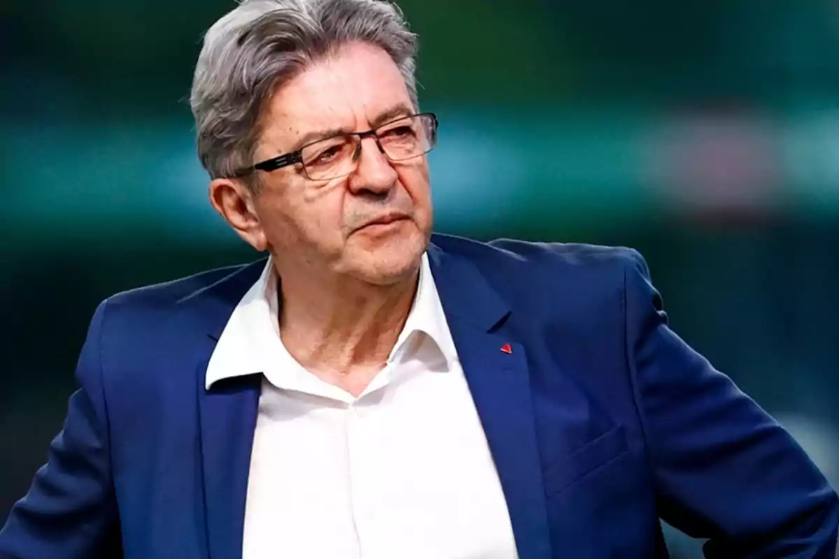 Hombre de cabello canoso y gafas vistiendo saco azul y camisa blanca mirando hacia un lado con expresión seria Hombre de cabello canoso y gafas vistiendo saco azul y camisa blanca mirando hacia un lado con expresión seria