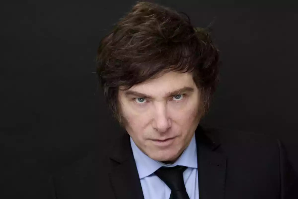 Brown-haired man with light eyes wearing a dark suit against a black background