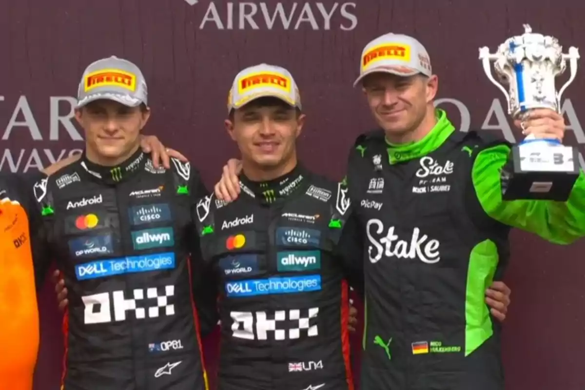 Three racing drivers pose smiling on the podium, two of them wearing black McLaren uniforms and the third in a black and green Sauber uniform, holding a silver trophy. Three racing drivers pose smiling on the podium, two of them wearing black McLaren uniforms and the third in a black and green Sauber uniform, holding a silver trophy.