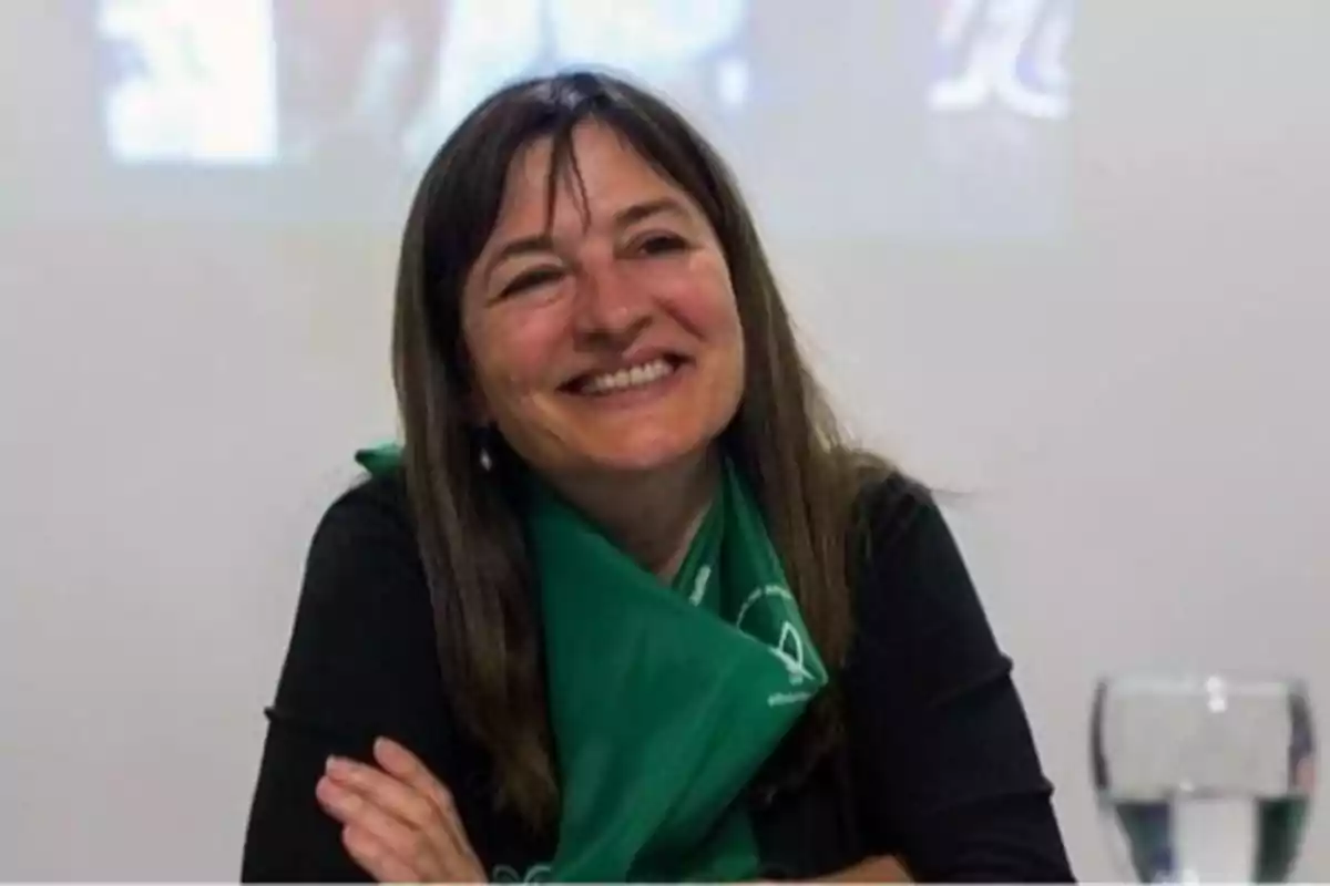 Mujer sonriente con cabello castaño y pañuelo verde sentada frente a un vaso de agua Mujer sonriente con cabello castaño y pañuelo verde sentada frente a un vaso de agua