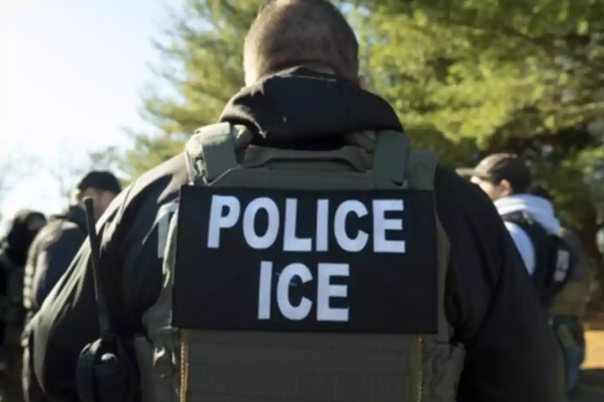 ICE police officer seen from behind wearing a bulletproof vest in an outdoor setting
