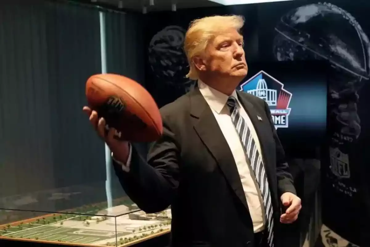 Hombre de traje sosteniendo un balón de fútbol americano en una exhibición relacionada con la NFL Hombre de traje sosteniendo un balón de fútbol americano en una exhibición relacionada con la NFL