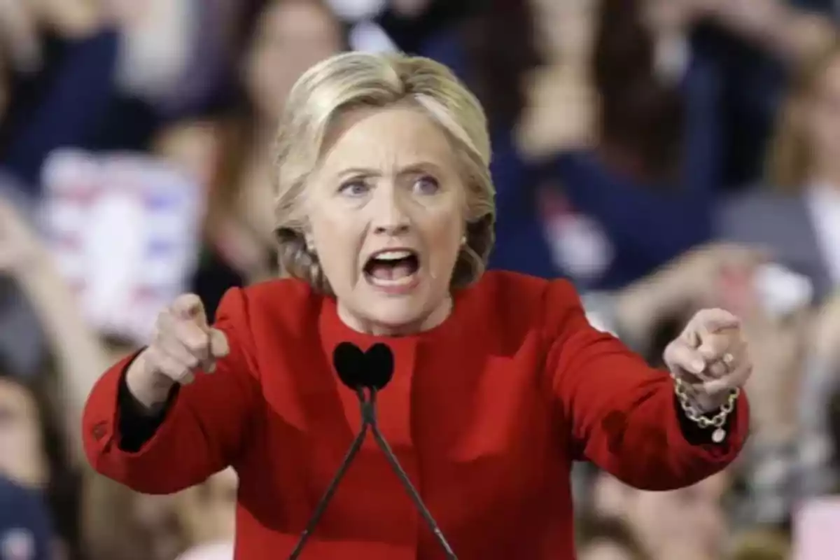 Blonde-haired woman in a red blazer speaking passionately and gesturing with both hands during a speech in front of a microphone Blonde-haired woman in a red blazer speaking passionately and gesturing with both hands during a speech in front of a microphone