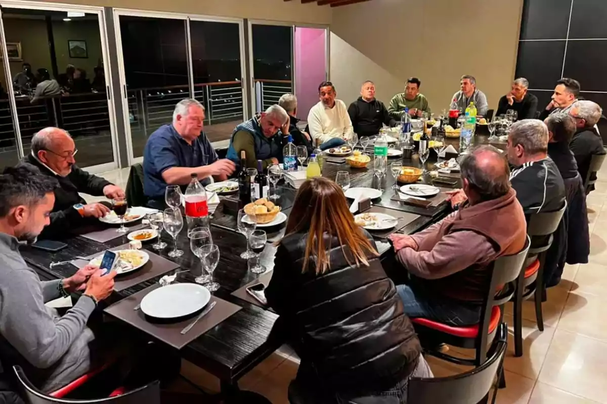 A group of people sitting around a large table sharing dinner in a modern indoor setting A group of people sitting around a large table sharing dinner in a modern indoor setting