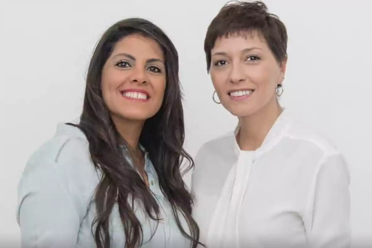 Dos mujeres sonrientes posan juntas frente a un fondo blanco Dos mujeres sonrientes posan juntas frente a un fondo blanco