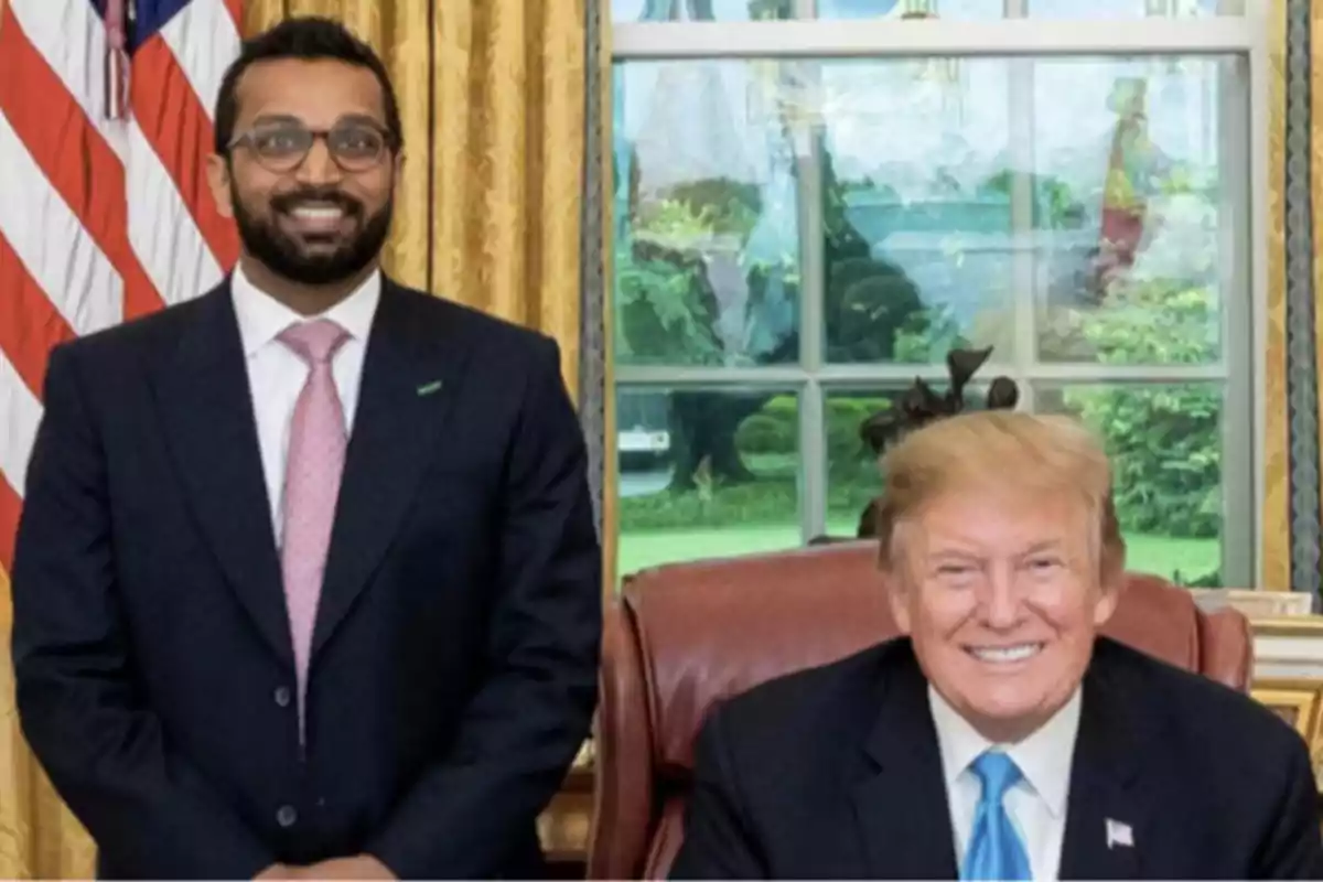 Two men in suits pose smiling in an elegant office with a United States flag in the background. Two men in suits pose smiling in an elegant office with a United States flag in the background.