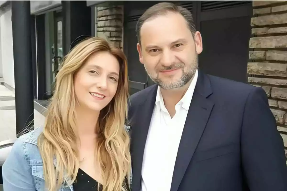 A blonde woman and a man with a short beard pose together and smile outdoors in front of a modern building. A blonde woman and a man with a short beard pose together and smile outdoors in front of a modern building.