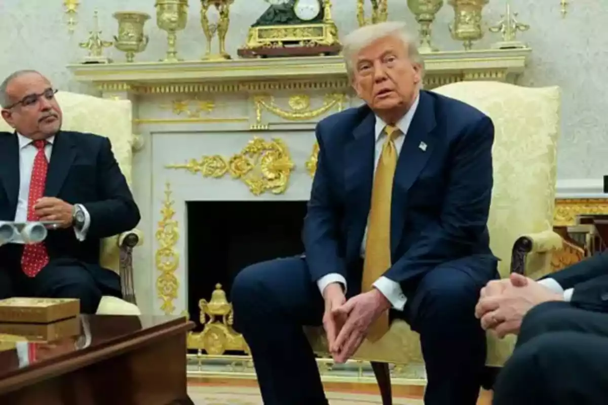 Three men in suits are talking in an elegant room decorated with golden details and a fireplace in the background. Three men in suits are talking in an elegant room decorated with golden details and a fireplace in the background.
