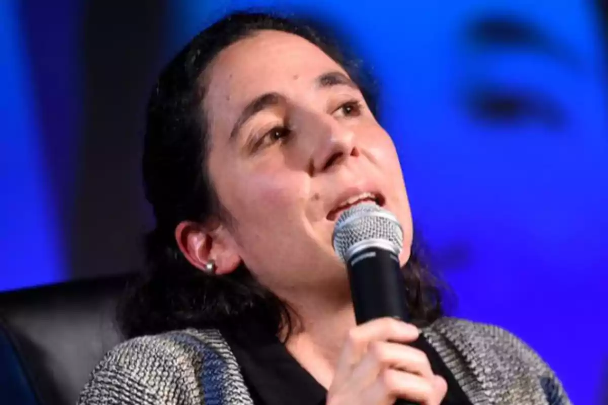 Dark-haired woman speaking while holding a microphone with a blurred blue background Dark-haired woman speaking while holding a microphone with a blurred blue background