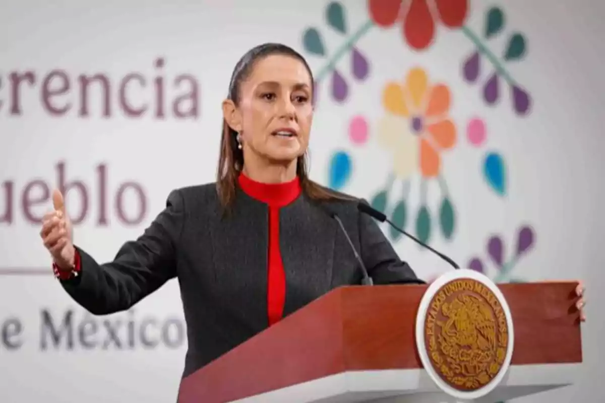 Mujer hablando en un podio oficial con el escudo de México al frente y un fondo decorativo colorido Mujer hablando en un podio oficial con el escudo de México al frente y un fondo decorativo colorido