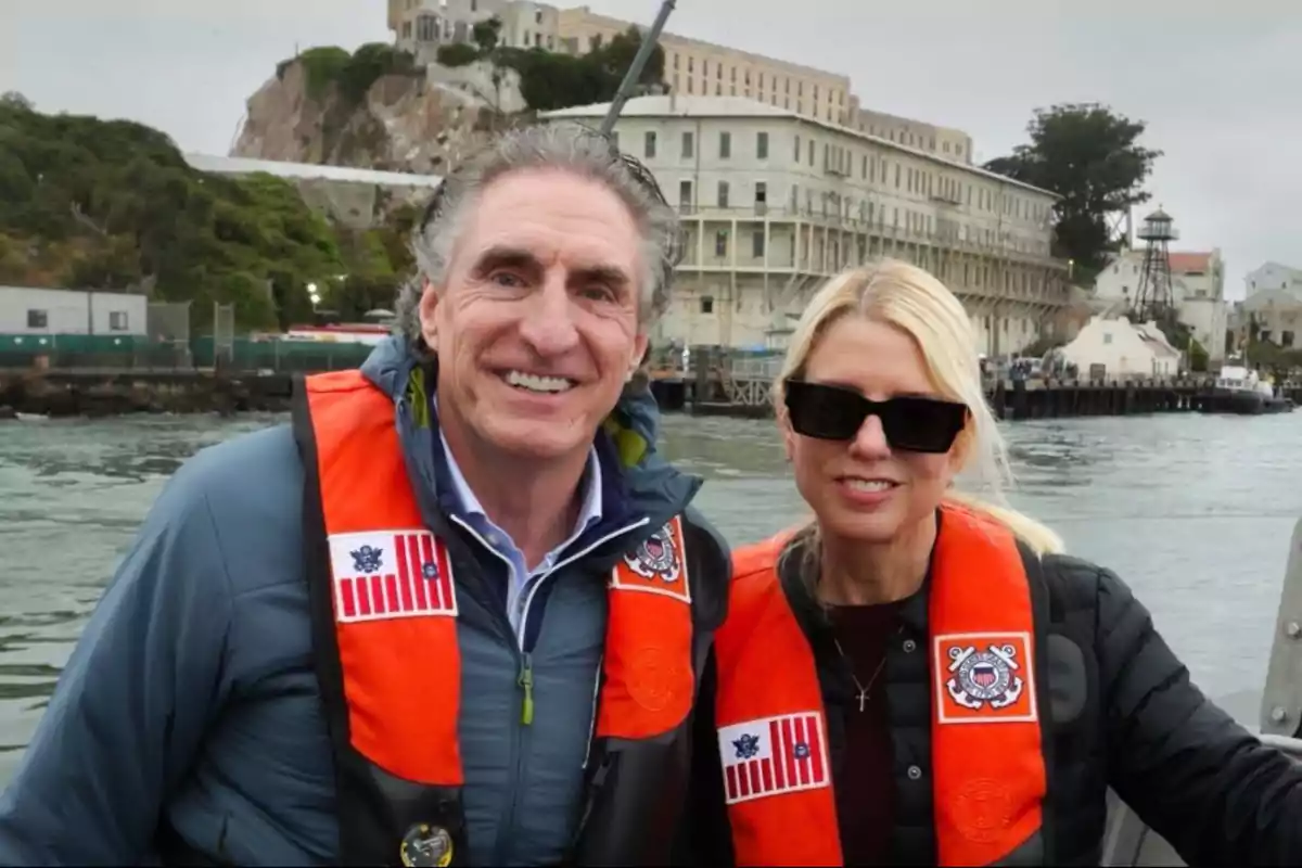 Dos personas con chalecos salvavidas naranjas posan sonrientes frente a la famosa prisión de Alcatraz, en un día nublado Dos personas con chalecos salvavidas naranjas posan sonrientes frente a la famosa prisión de Alcatraz, en un día nublado