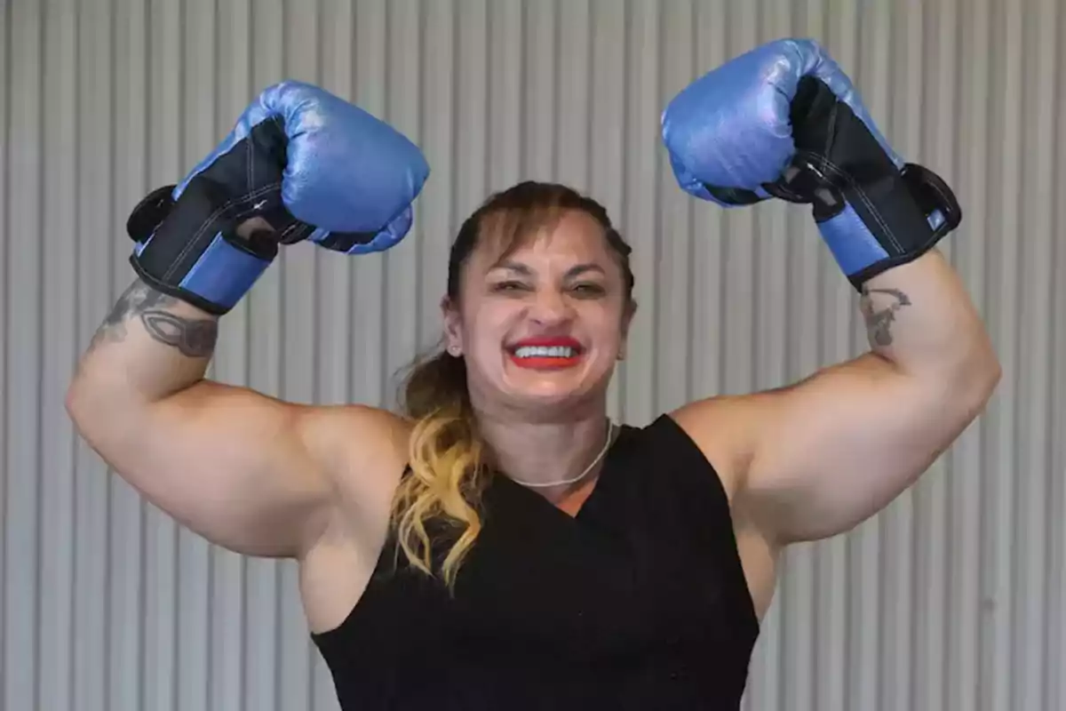 Smiling woman with blue boxing gloves showing her muscles and wearing a black t-jersey Smiling woman with blue boxing gloves showing her muscles and wearing a black t-jersey