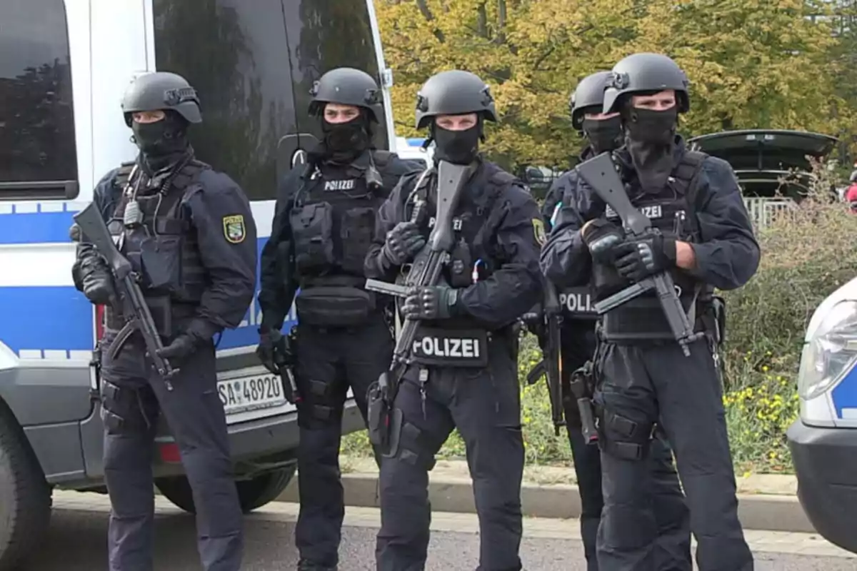 Cinco policías fuertemente armados con uniforme táctico y chalecos antibalas están de pie junto a una patrulla policial Cinco policías fuertemente armados con uniforme táctico y chalecos antibalas están de pie junto a una patrulla policial