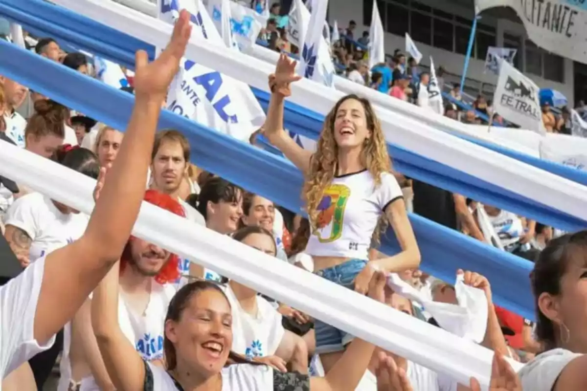 Personas celebrando en una multitud con banderas y tiras de tela blancas y azules en un estadio
