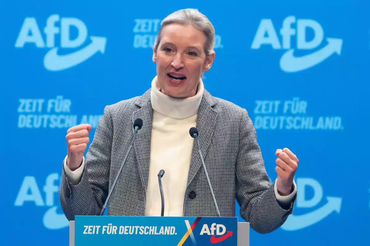 Mujer hablando en un podio con fondo azul y logotipos de AfD Mujer hablando en un podio con fondo azul y logotipos de AfD