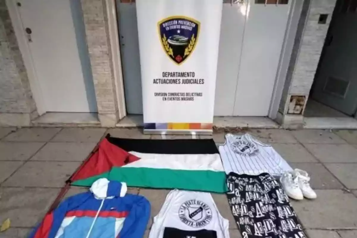 Sportswear, a flag, and a pair of sneakers displayed on the floor in front of a police sign that reads Judicial Proceedings Department