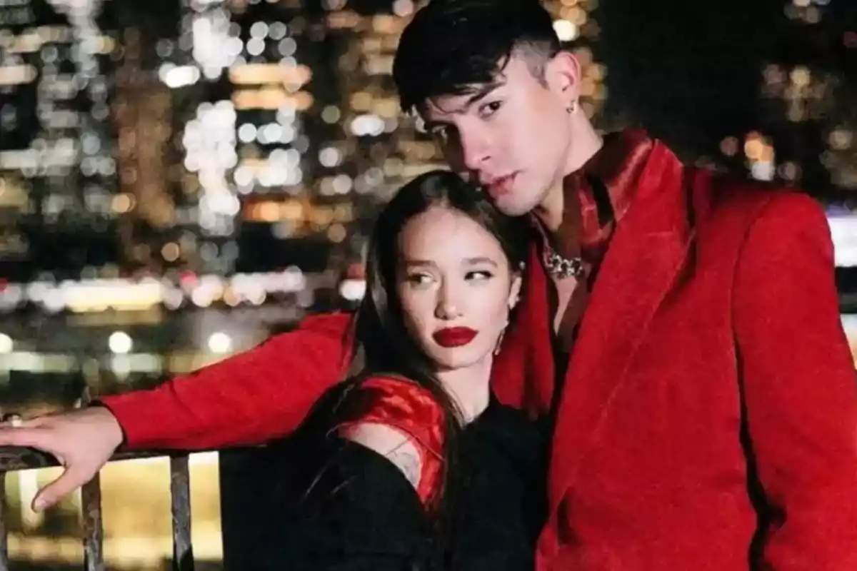 Couple posing at night in front of a lit-up city, both wearing elegant clothes and the man wearing a red blazer. Couple posing at night in front of a lit-up city, both wearing elegant clothes and the man wearing a red blazer.