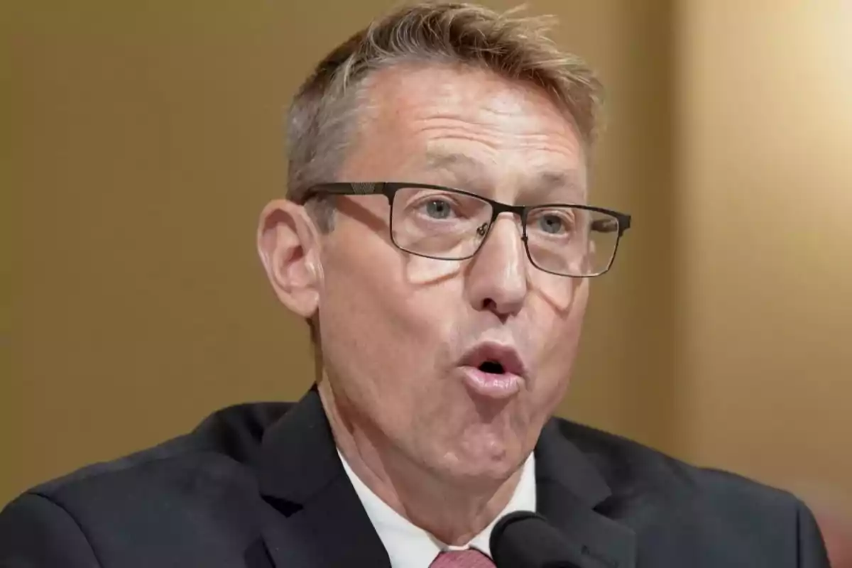 Short-haired man with glasses speaking in front of a microphone with a serious expression Short-haired man with glasses speaking in front of a microphone with a serious expression