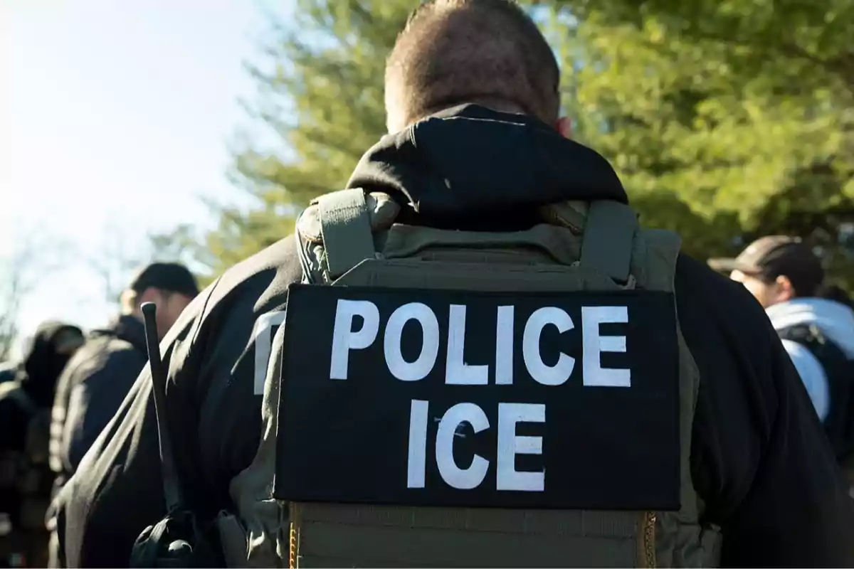 ICE police officer seen from behind wearing a bulletproof vest and radio in an outdoor setting ICE police officer seen from behind wearing a bulletproof vest and radio in an outdoor setting