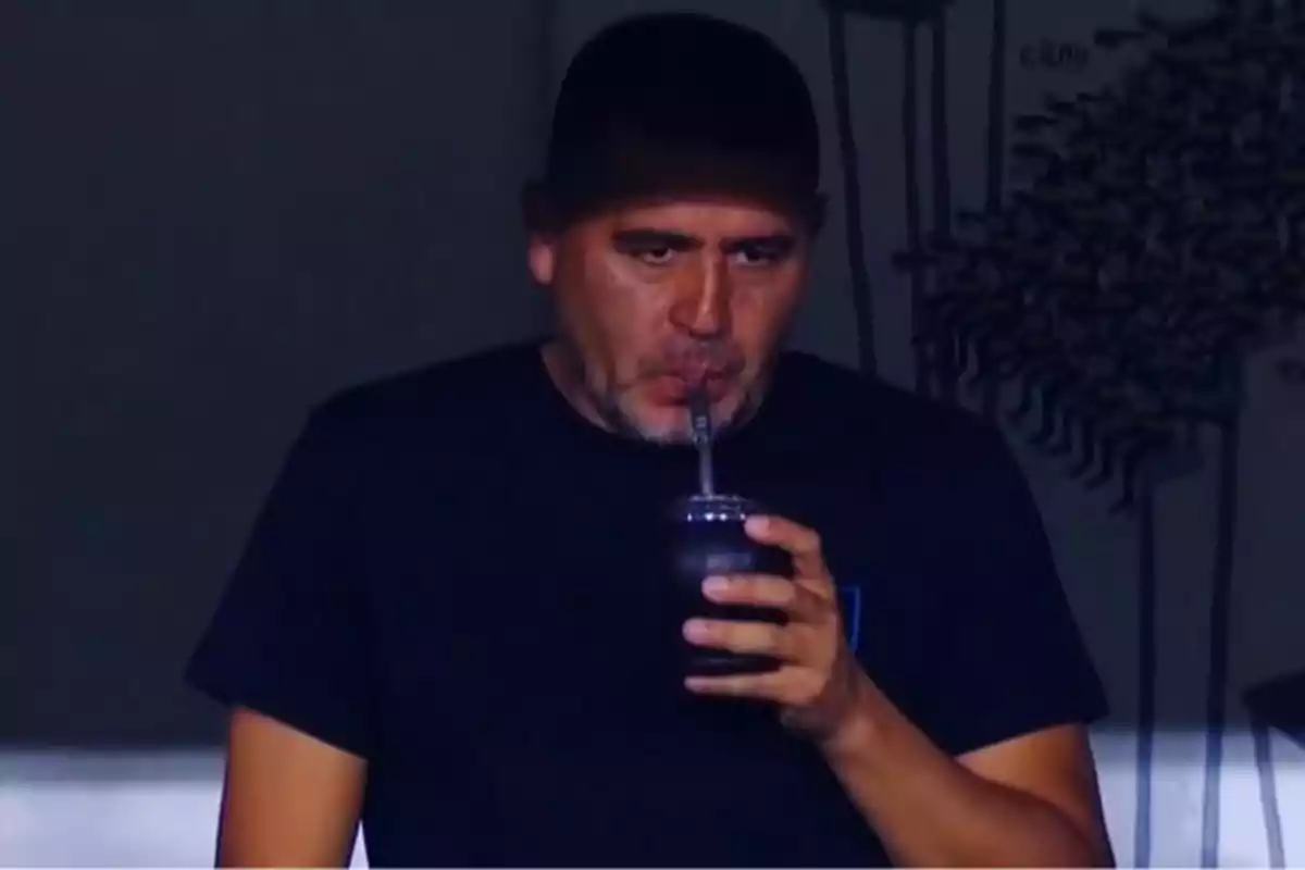 Man in a dark jersey drinking mate with a serious expression