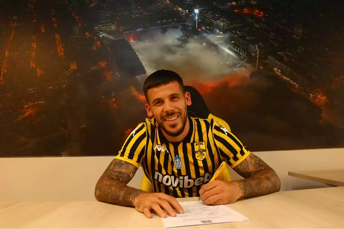 Soccer player wearing a yellow and black jersey signing a contract while smiling in front of an aerial image of a lit-up stadium Soccer player wearing a yellow and black jersey signing a contract while smiling in front of an aerial image of a lit-up stadium